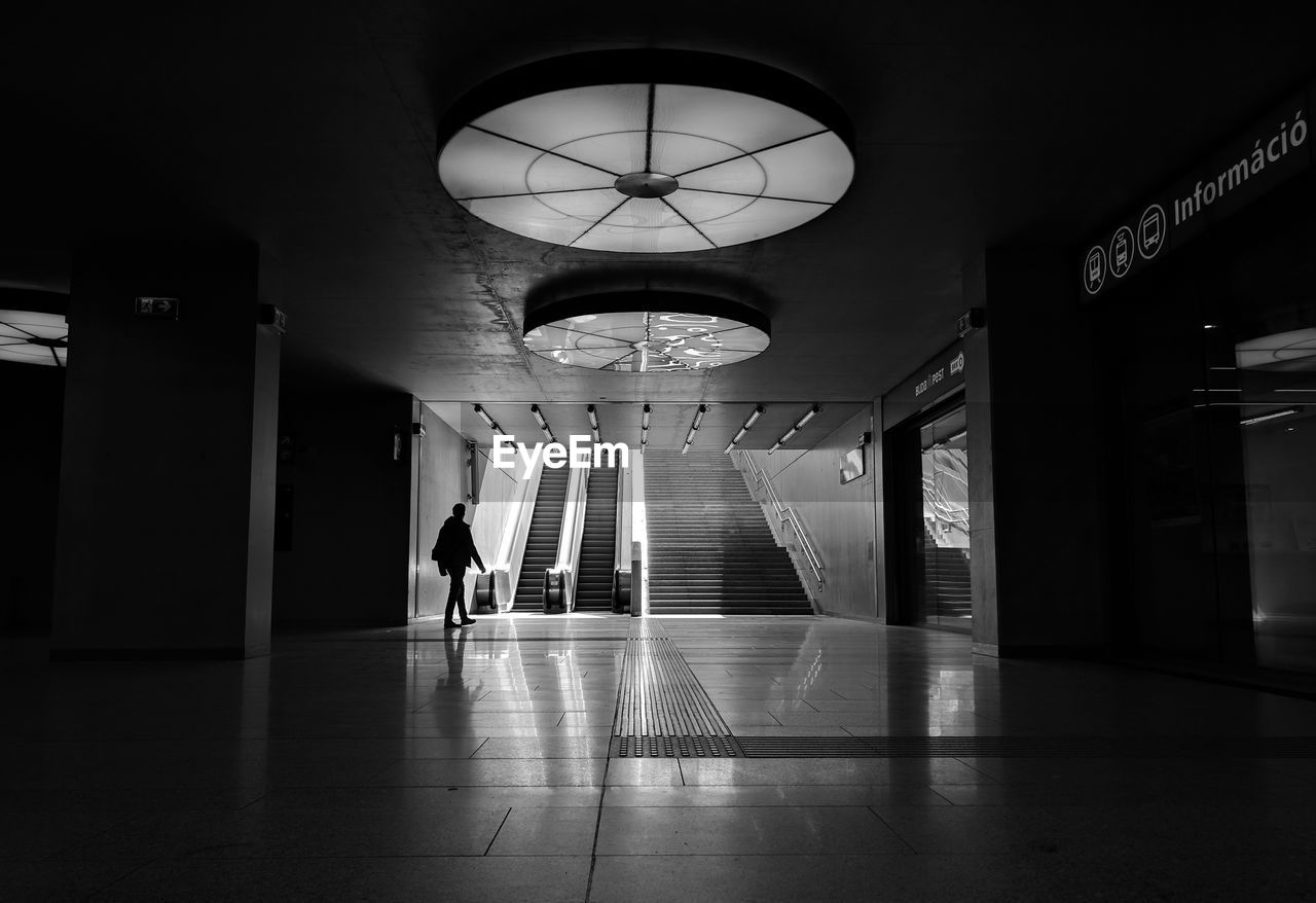 MAN WALKING ON ILLUMINATED CORRIDOR OF BUILDING