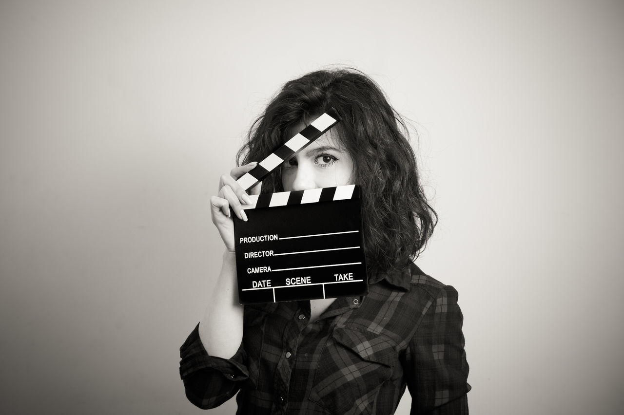 Portrait of beautiful woman holding clapboard against wall