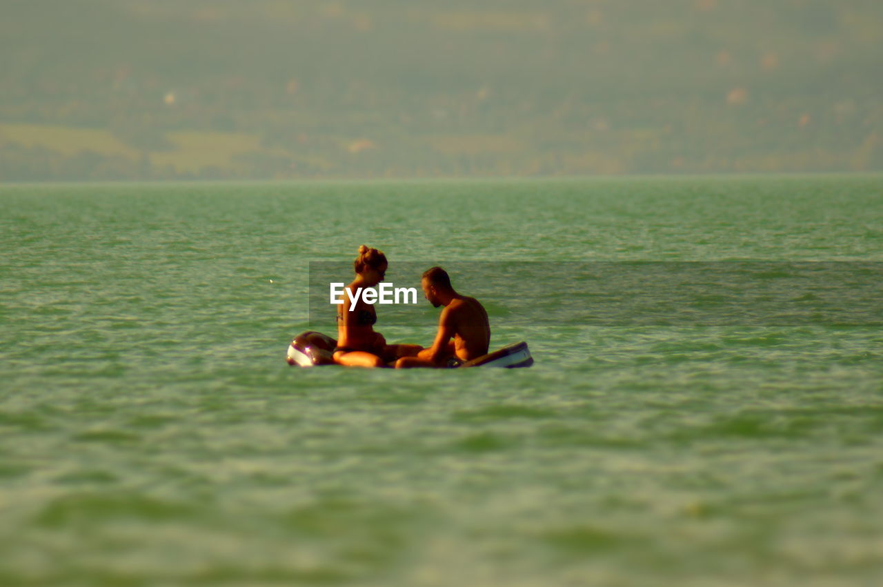 REAR VIEW OF FRIENDS SITTING ON SEA SHORE