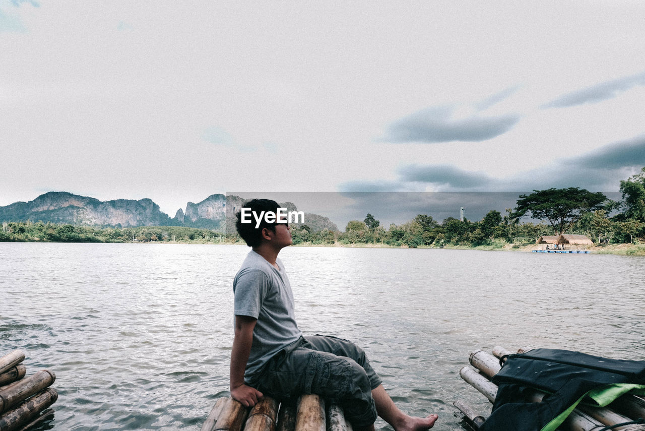 Man sitting on wooden raft over lake against sky