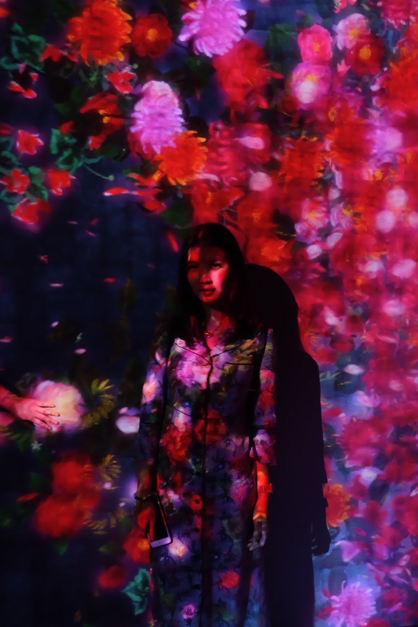 PORTRAIT OF BEAUTIFUL YOUNG WOMAN STANDING AGAINST ILLUMINATED PLANTS