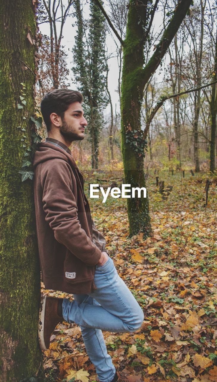 Young man leaning on tree in forest