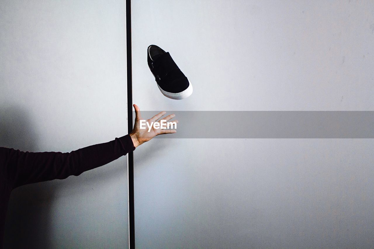 Cropped image of hand throwing shoe against wall