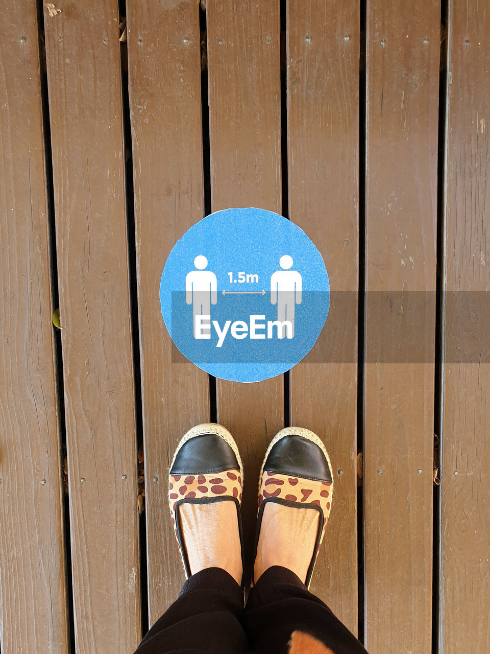Low section of person standing over social distancing sign on wooden floor