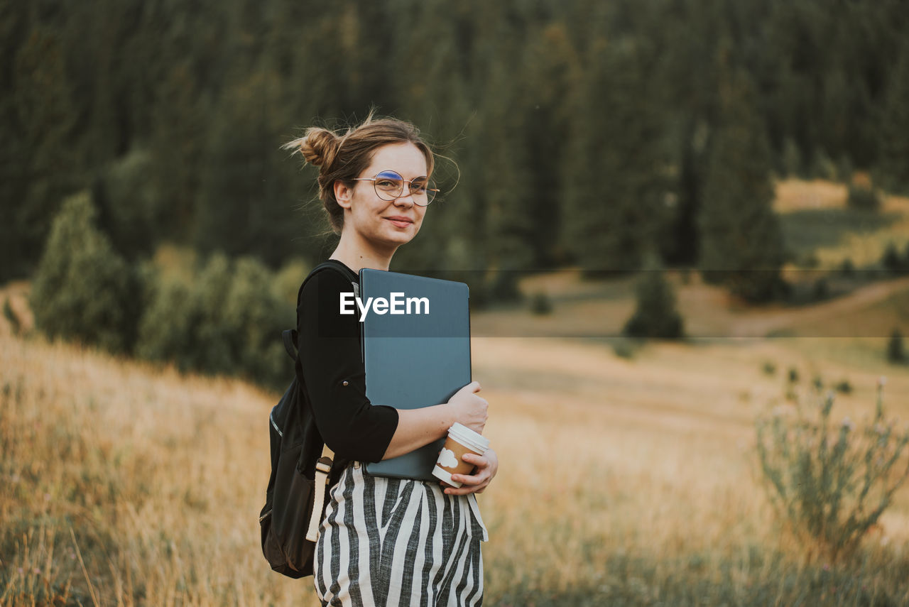 Happy woman freelancer with glasses working on laptop, remote location in nature