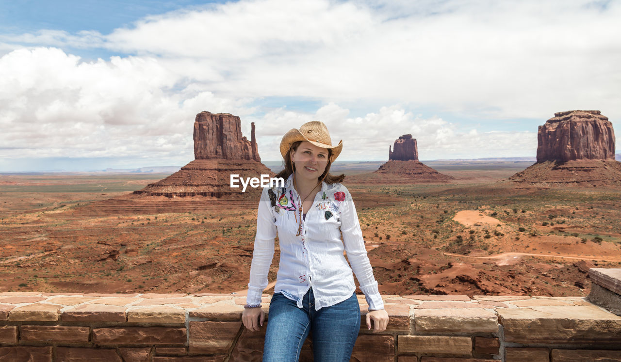 WOMAN STANDING ON ROCK AGAINST CLOUDY SKY