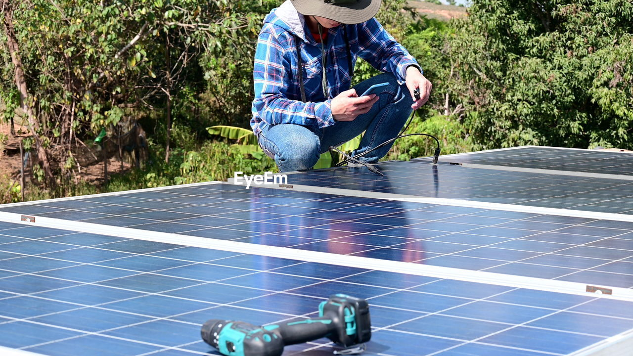Low section of worker using mobile phone while installing solar panel