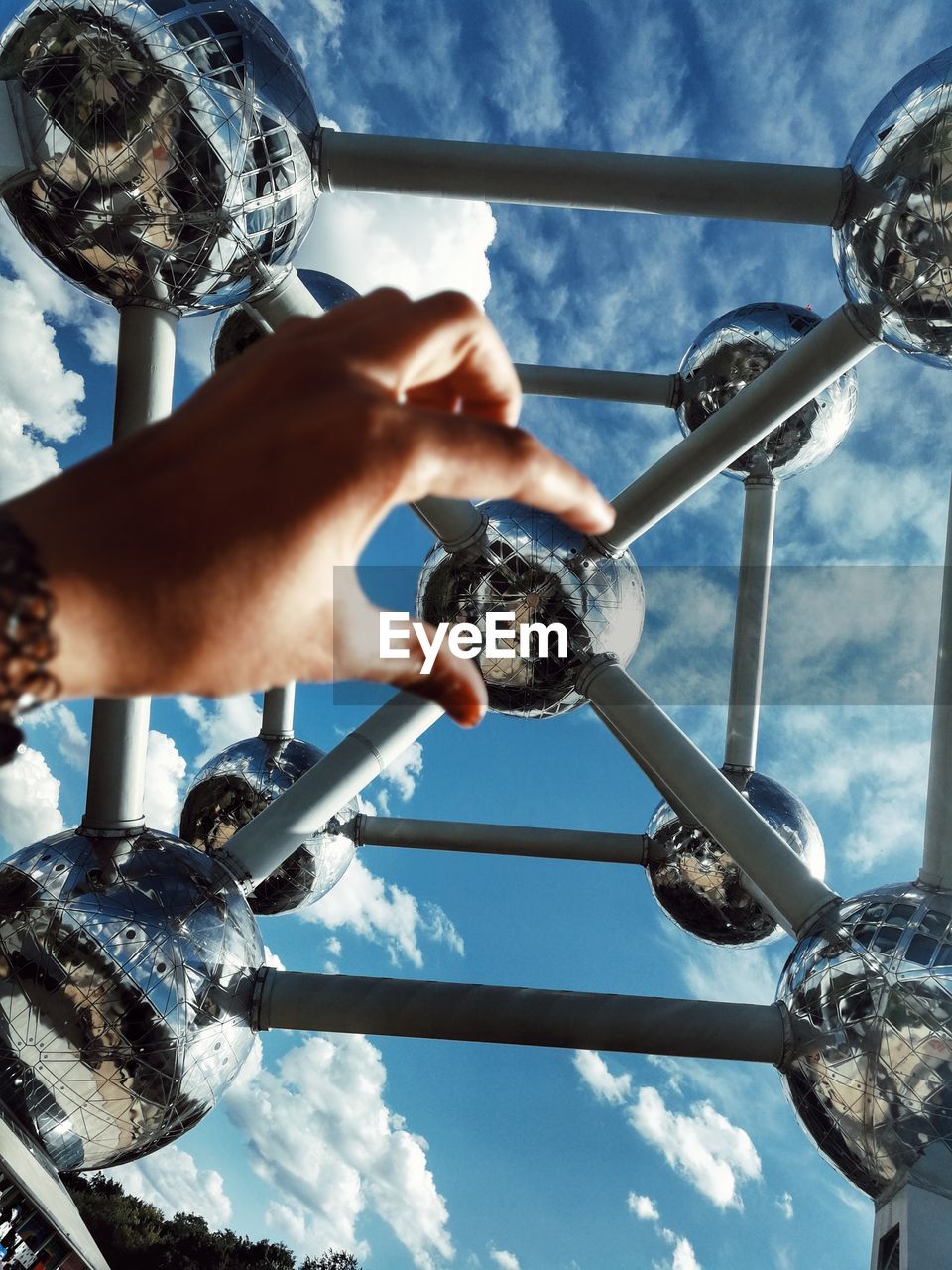 LOW ANGLE VIEW OF PERSON HAND HOLDING METALLIC STRUCTURE AGAINST SKY