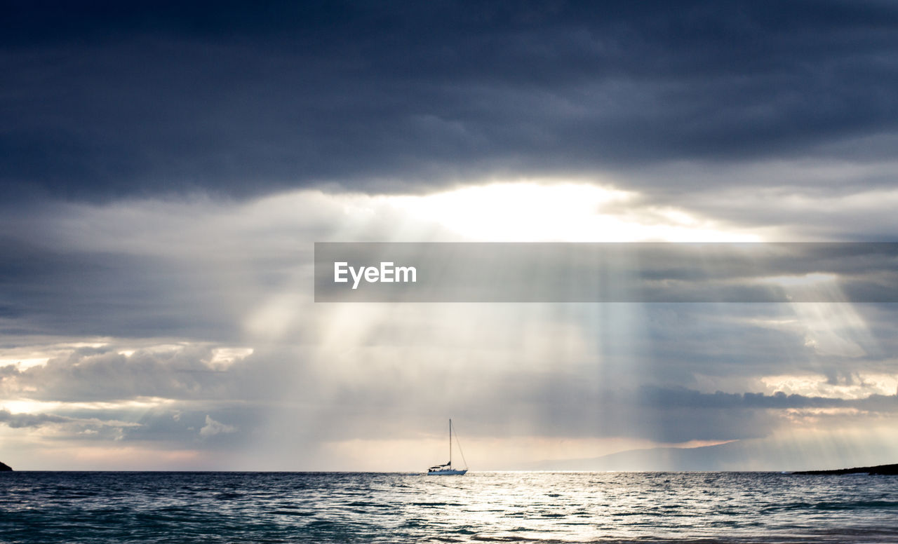 Idyllic shot of cloudy sky with sunbeam over sailboat in sea