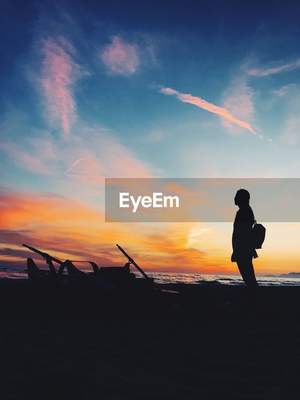 Silhouette woman standing at beach against sky during sunset