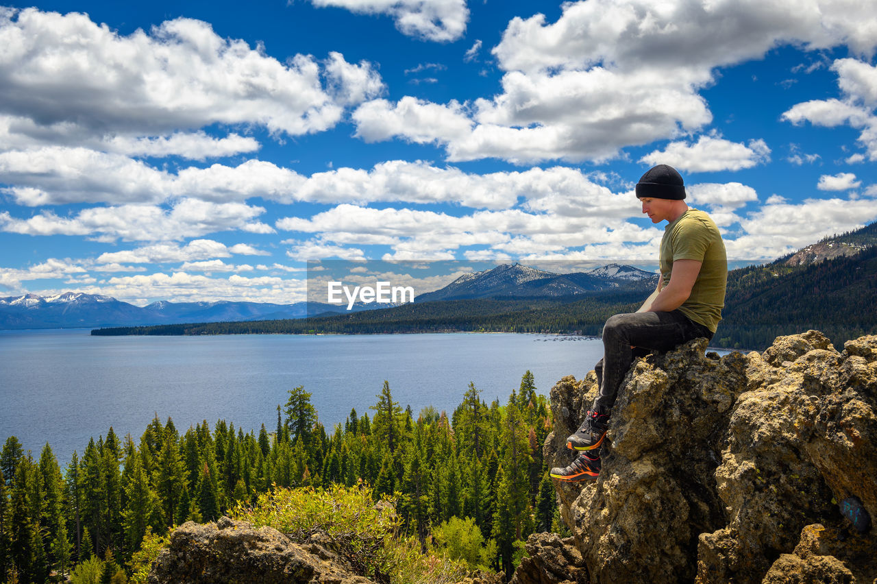 rear view of woman standing on rock by lake against sky