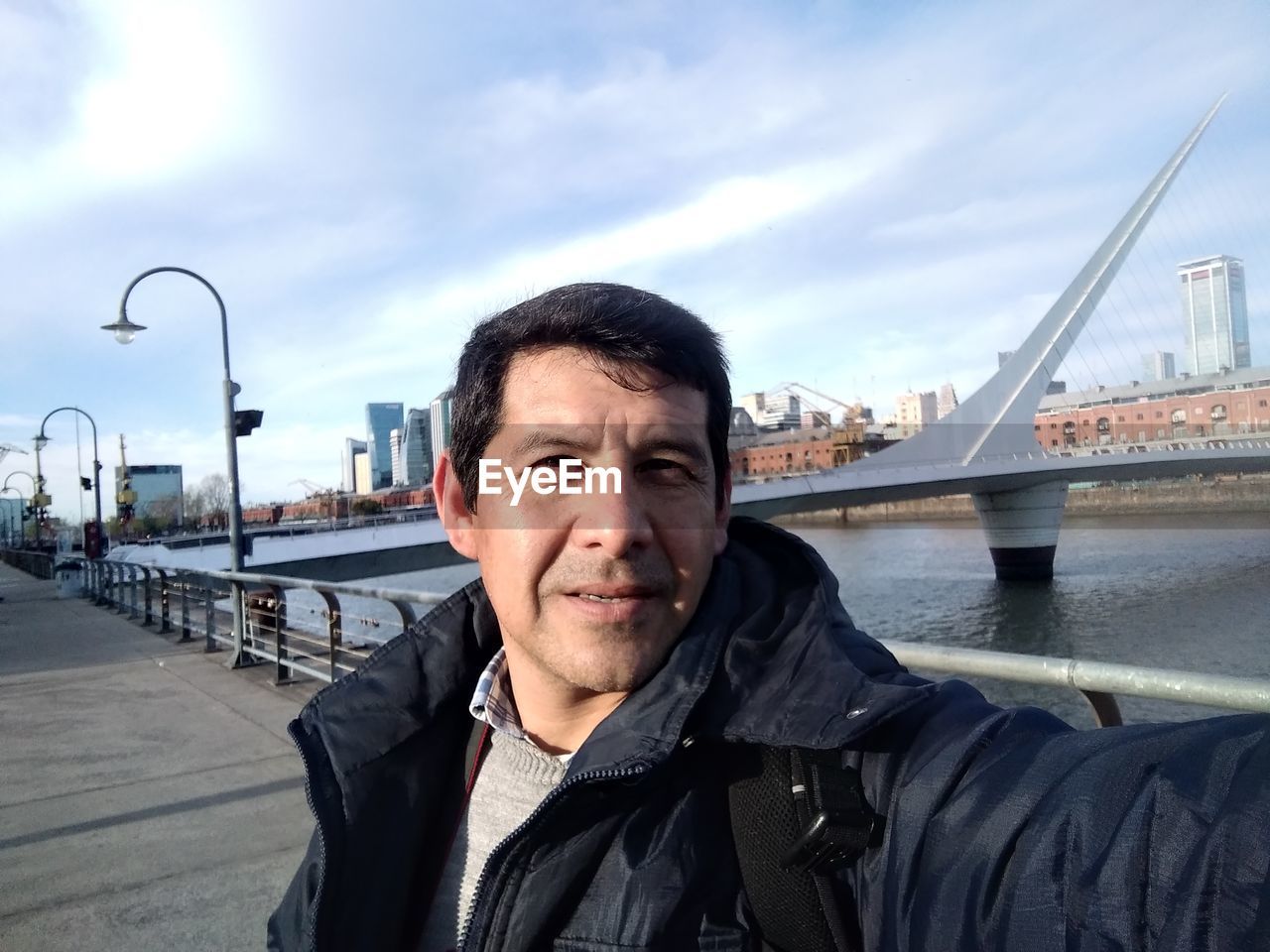 PORTRAIT OF MATURE MAN SITTING ON BRIDGE OVER RIVER