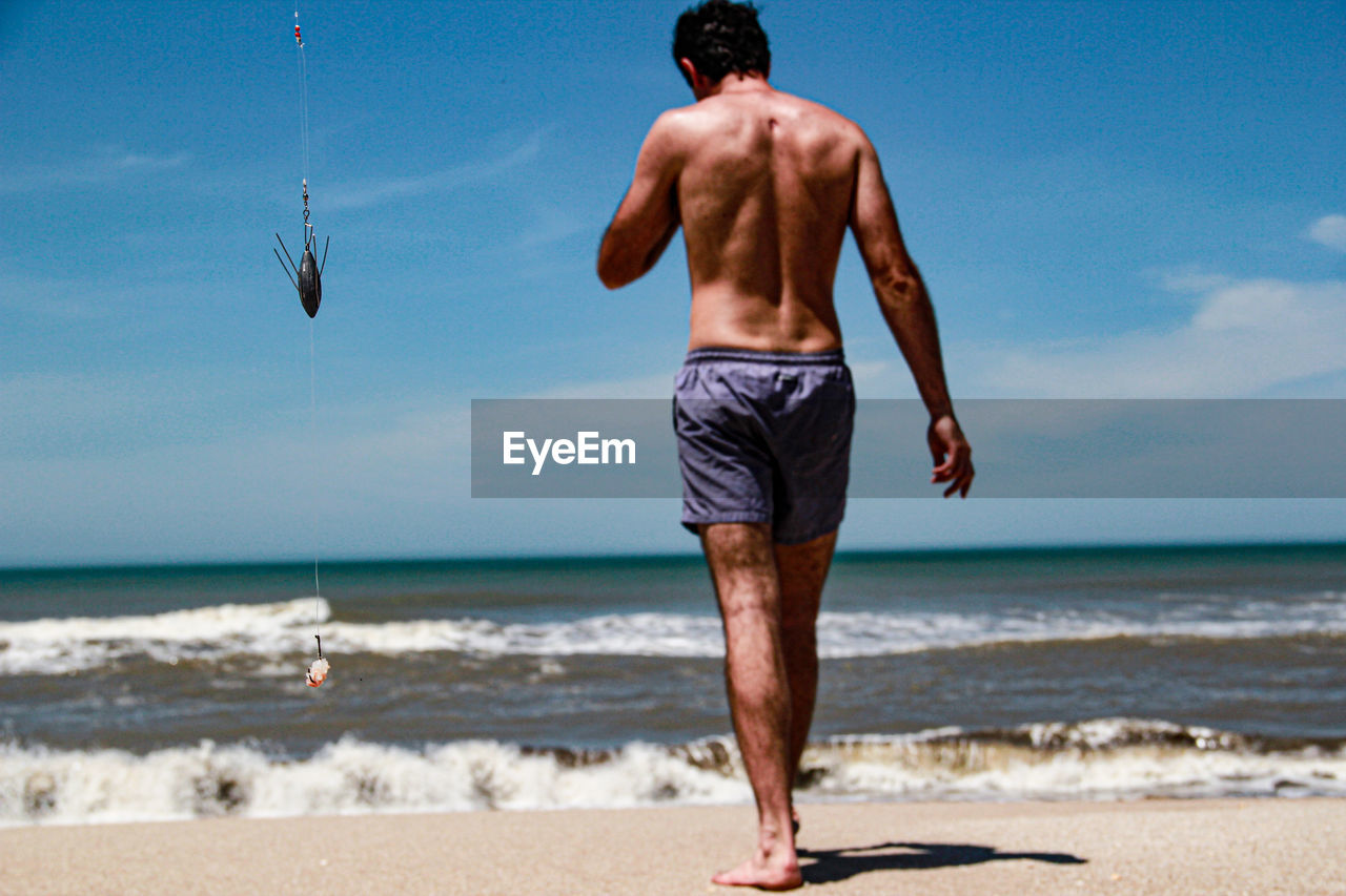 Rear view of shirtless man walking on beach