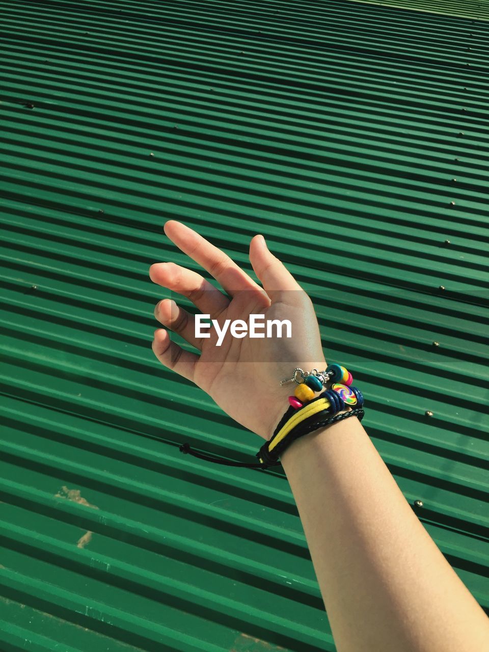 Cropped hand by green corrugated iron