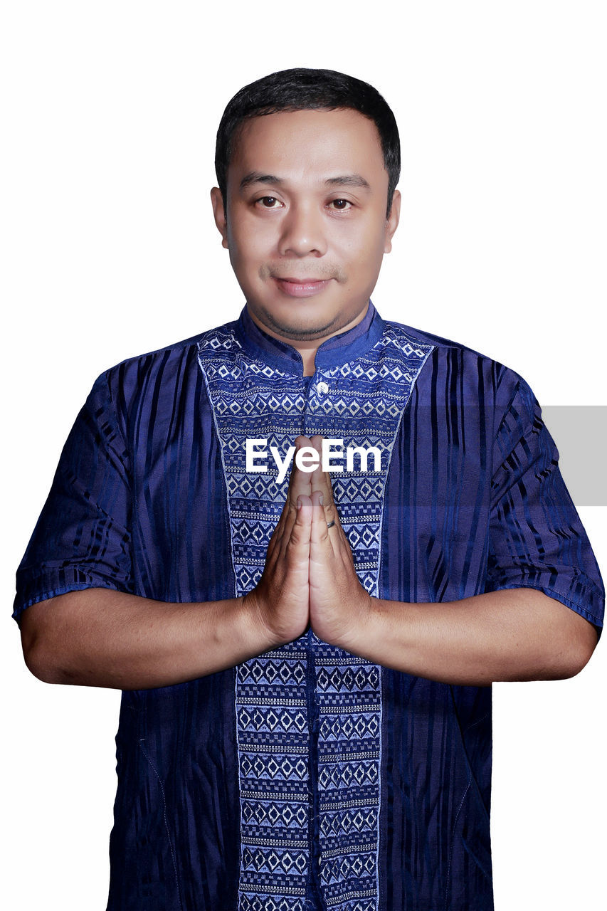 Portrait of man with hands clasped standing against white background