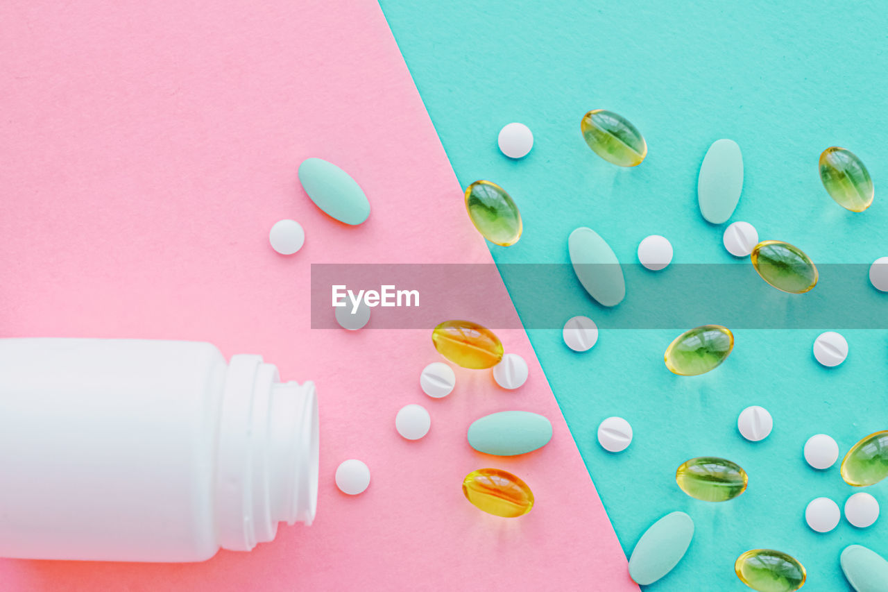 directly above shot of pills spilling from bottle and medicines on pink background