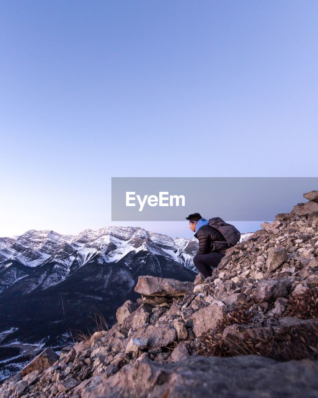 Man sitting on rock against clear blue sky