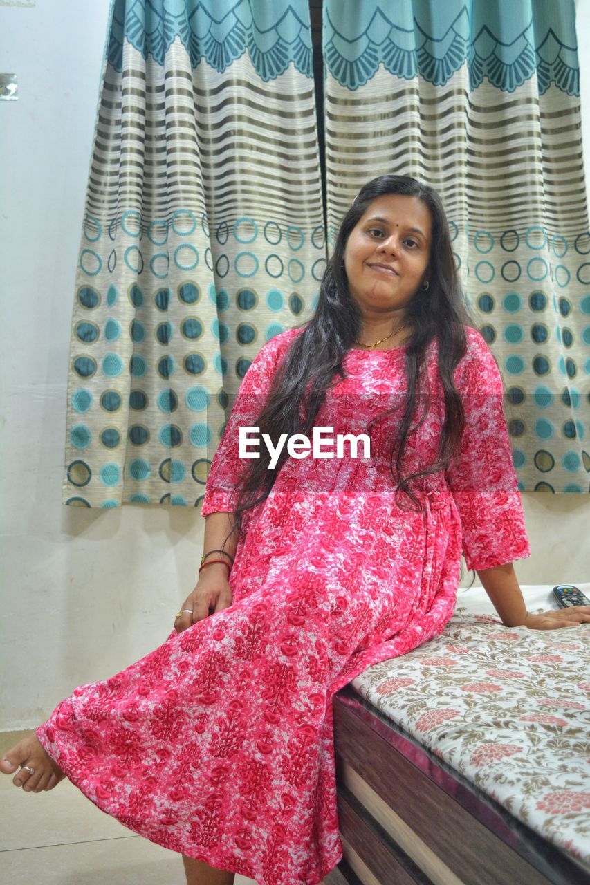 one person, pink, women, smiling, pattern, looking at camera, textile, portrait, clothing, dress, adult, happiness, standing, indoors, front view, lifestyles, three quarter length, emotion, young adult, hairstyle, female, fashion, long hair, leisure activity, curtain, cheerful, casual clothing, red, art, black hair, photo shoot, brown hair, pattern (fashion design), looking