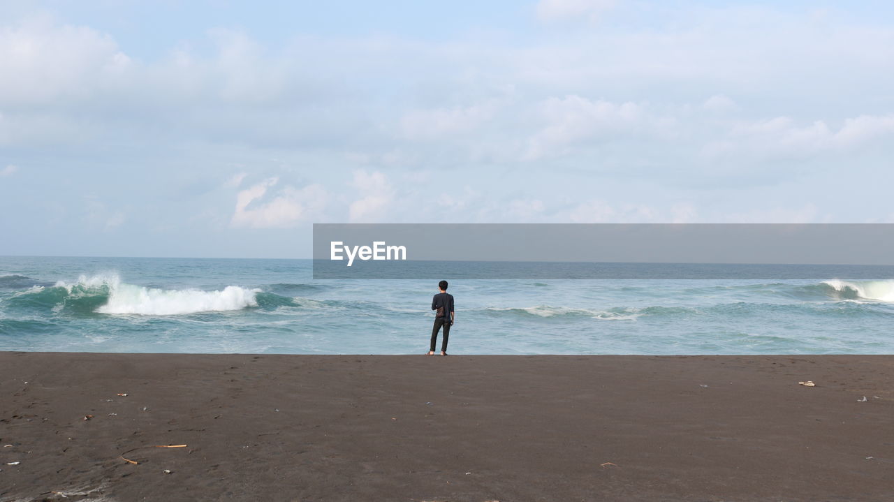 Rear view of man alone standing at beach against sky