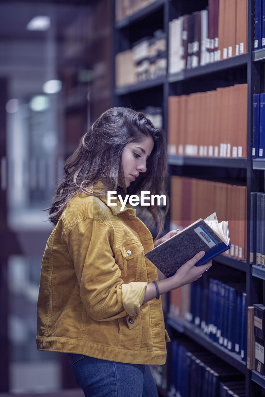 Side view of young woman reading book in library