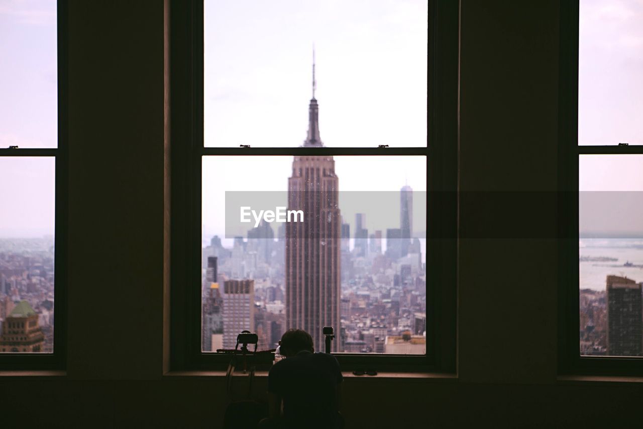 Person sitting on chair by window against empire state building