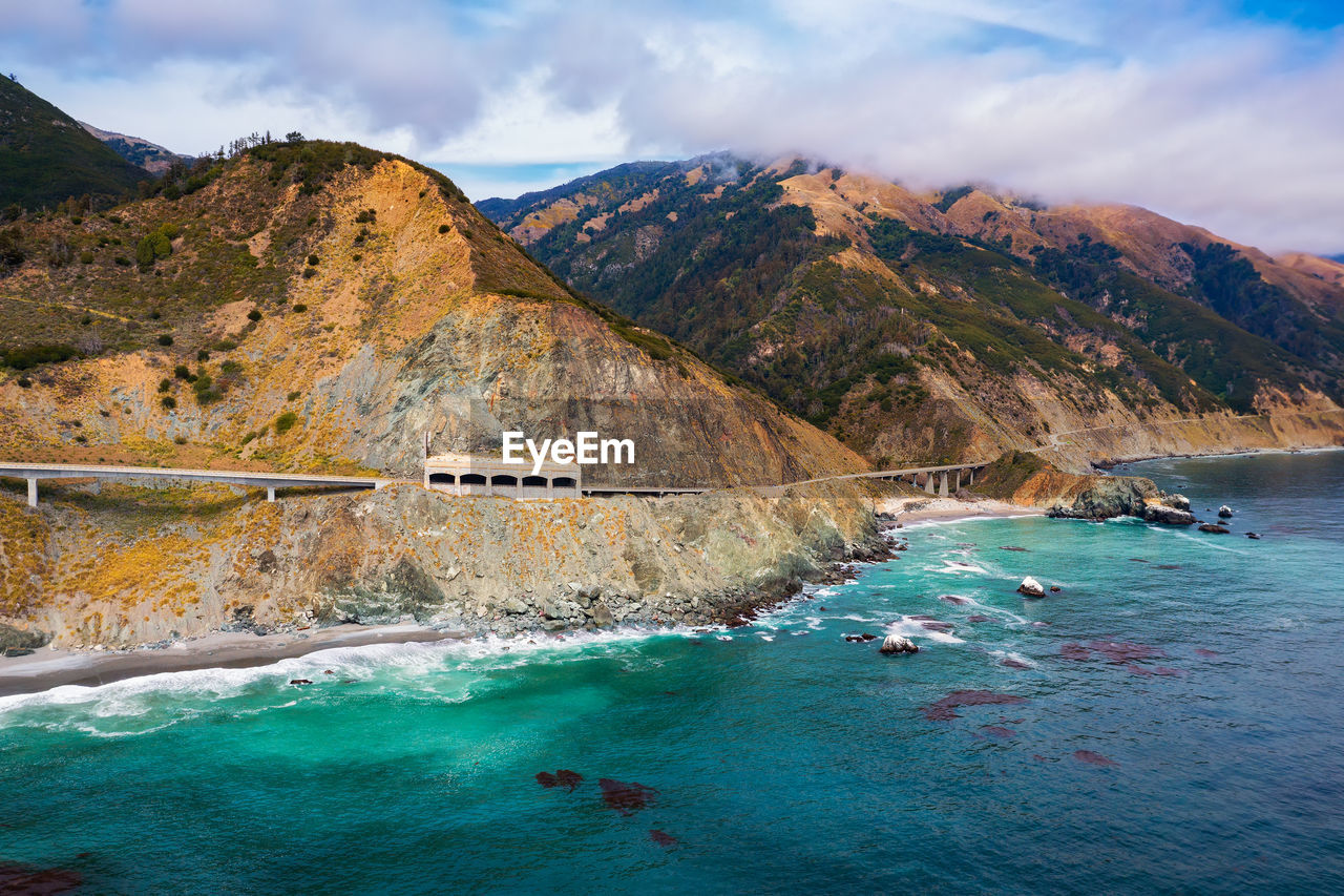 scenic view of sea by mountains against sky