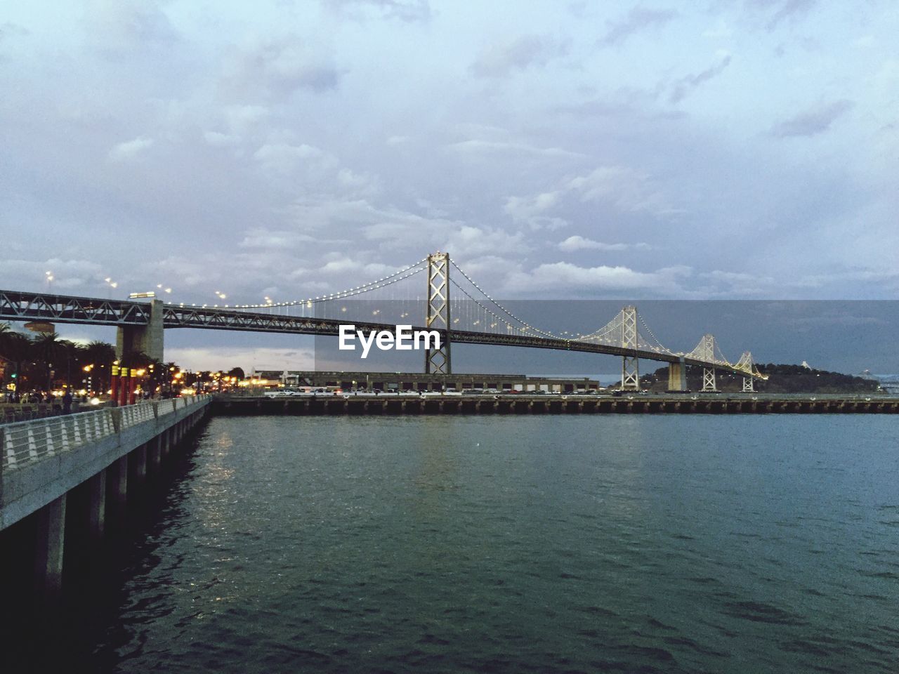 Bay bridge over river against cloudy sky