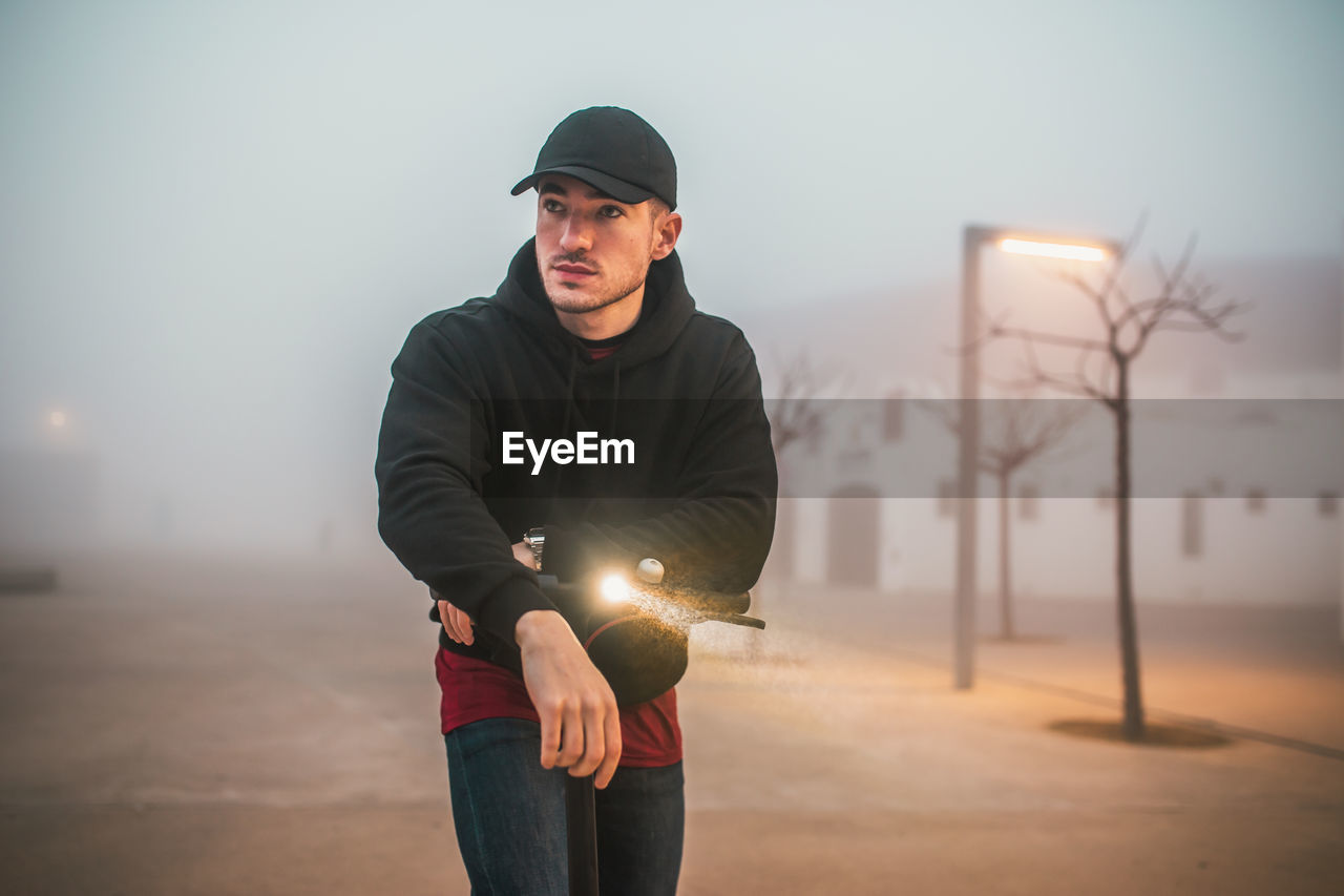 Man with cap on electric scooter during a foggy day