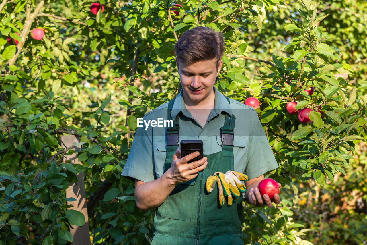 portrait of young man using mobile phone while standing against plants