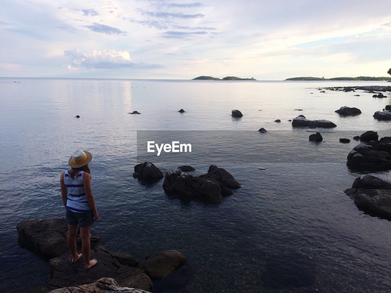 Rear view of woman standing on rock at sea against sky