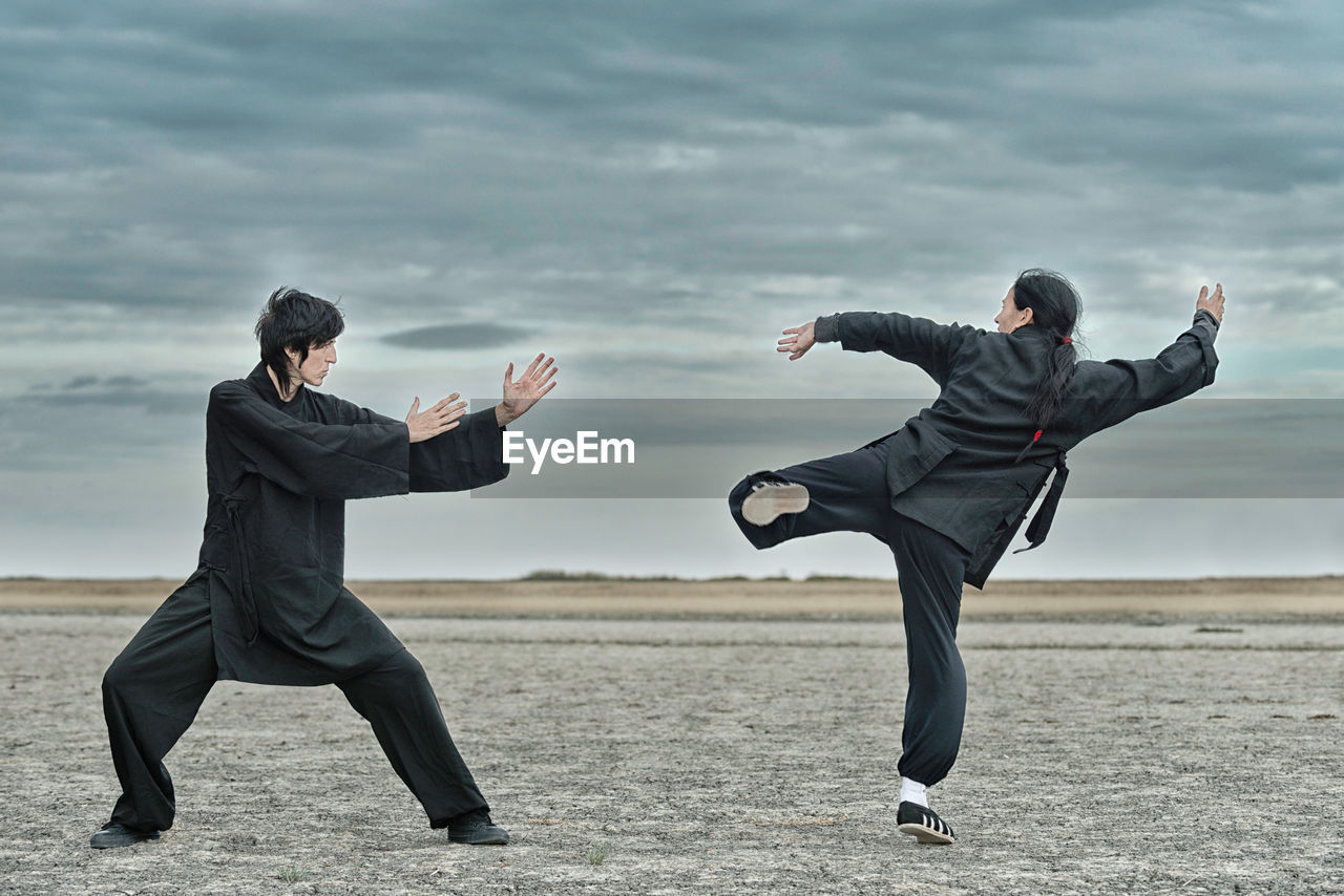 People practicing martial arts on land against cloudy sky