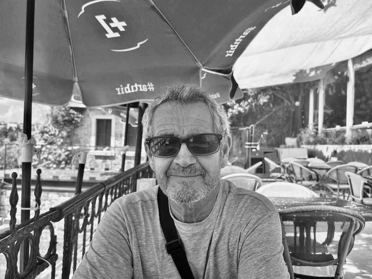 portrait, one person, adult, sunglasses, glasses, men, front view, black and white, leisure activity, looking at camera, lifestyles, fashion, monochrome, day, casual clothing, monochrome photography, smiling, mature adult, headshot, architecture, senior adult, outdoors, waist up, clothing, sitting, cafe, vehicle, seat, nature, happiness, transportation, person, restaurant