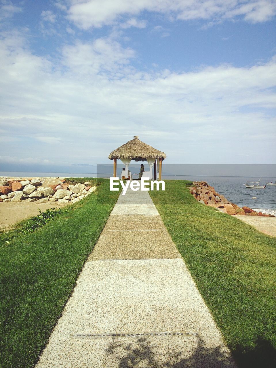 Footpath by sea against cloudy sky