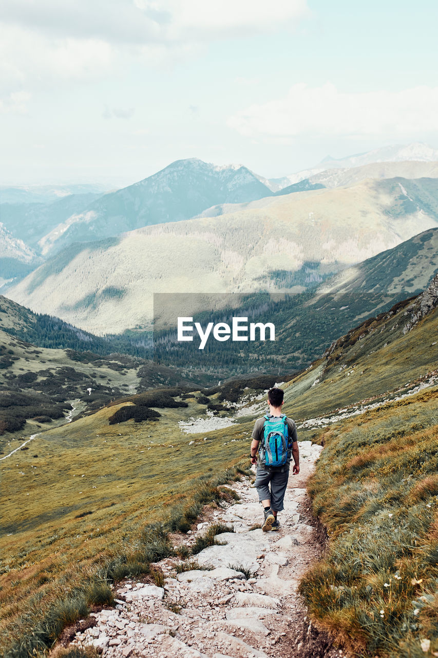 Young man with backpack hiking in a mountains, actively spending summer vacation