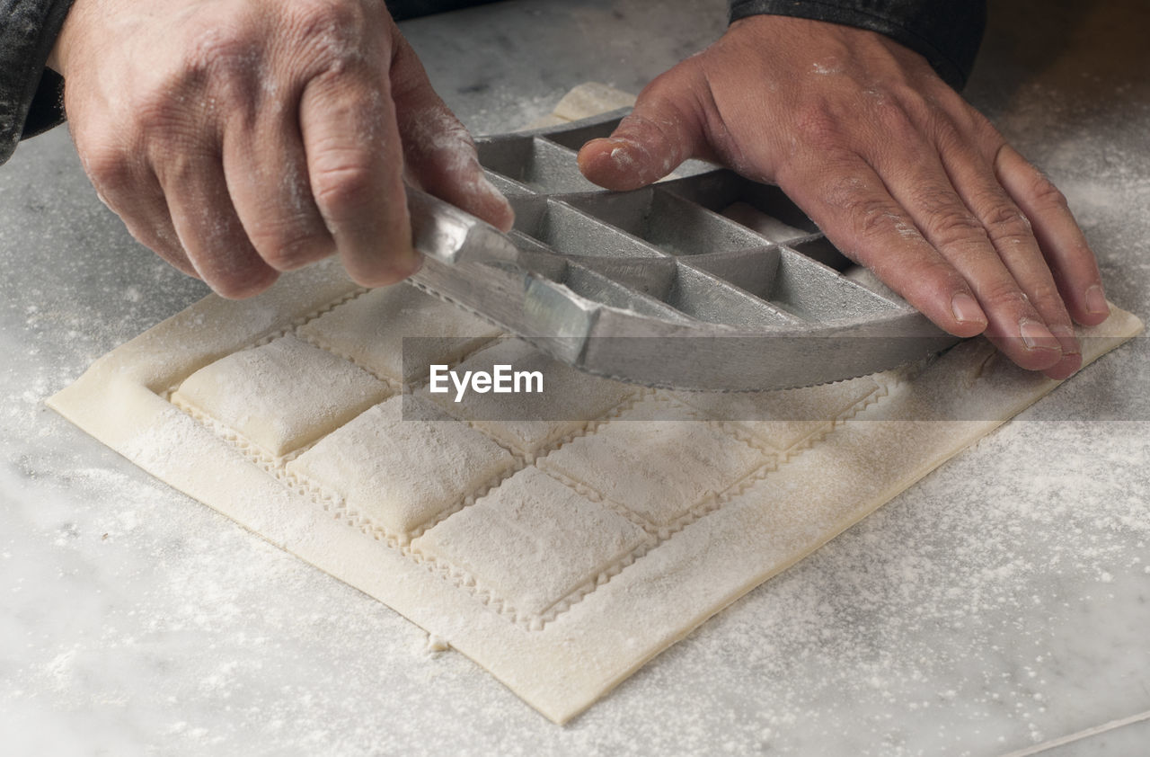 Cropped hands of chef cutting dough on table in commercial kitchen