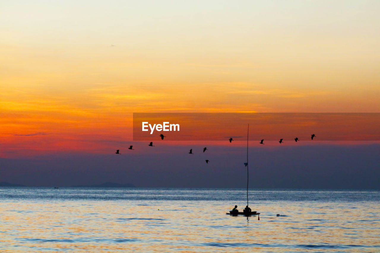 Silhouette people on sea against sky during sunset