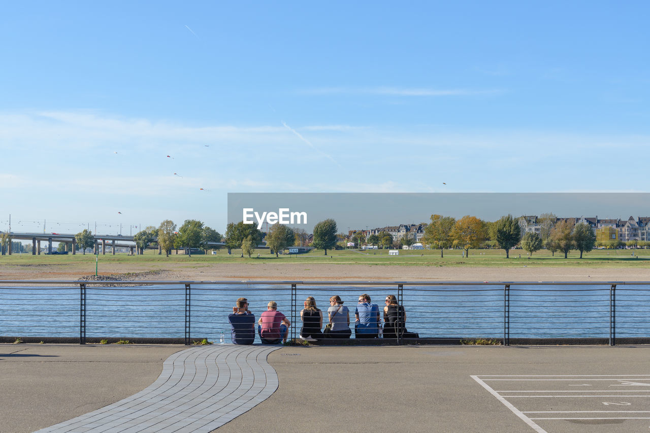 Group of people sitting on outer railing side along riverside of rhine river in düsseldorf, germany.