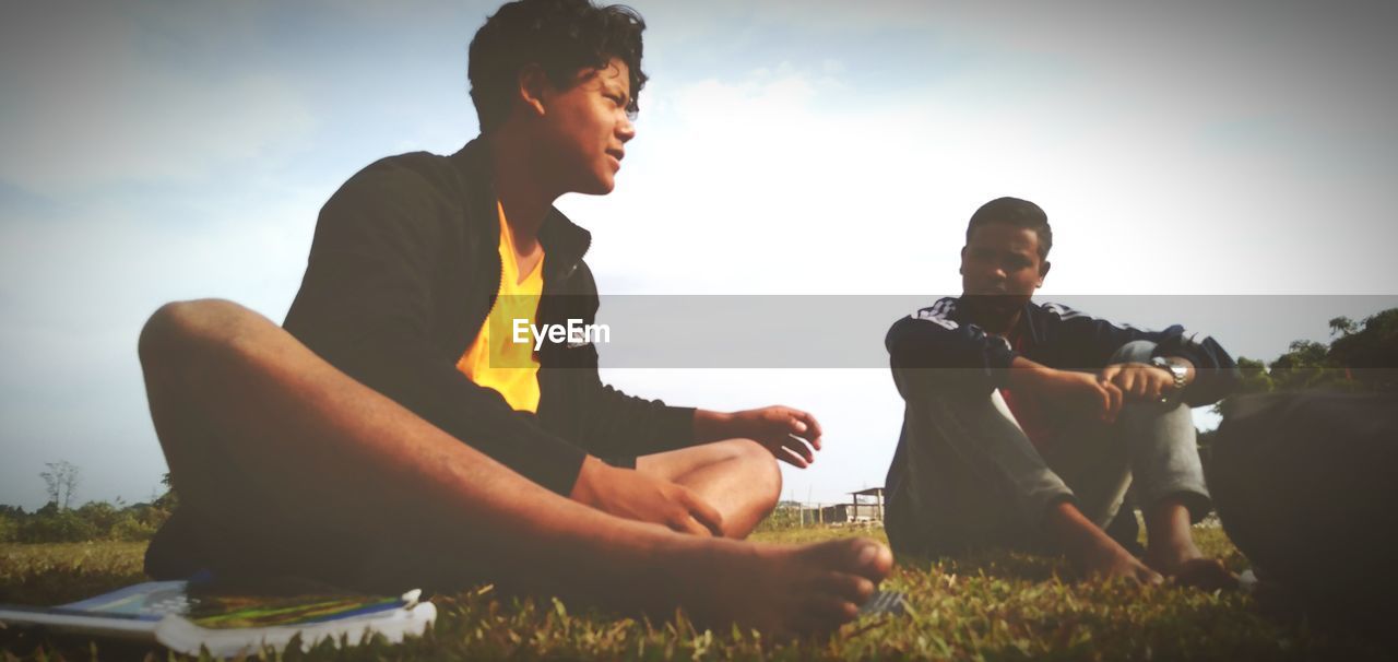 MAN SITTING ON FIELD AGAINST SKY