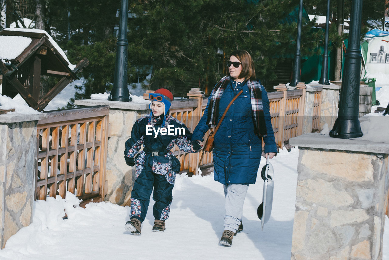 Full length of mother and son holding hands while walking on road during winter