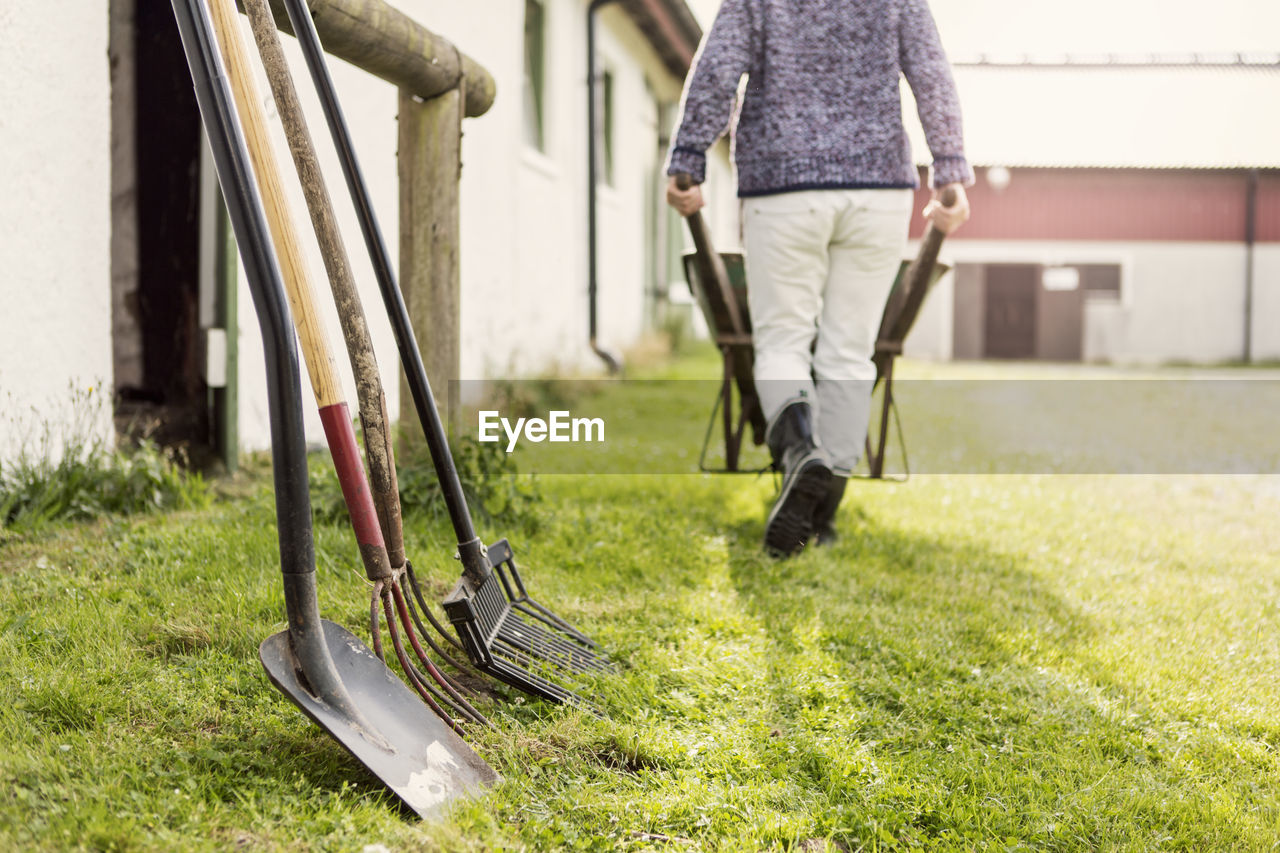 Work tools arranged by barn while woman pushing wheelbarrow at farm