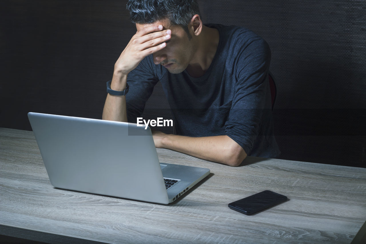 High angle view of tired man sitting by laptop at table