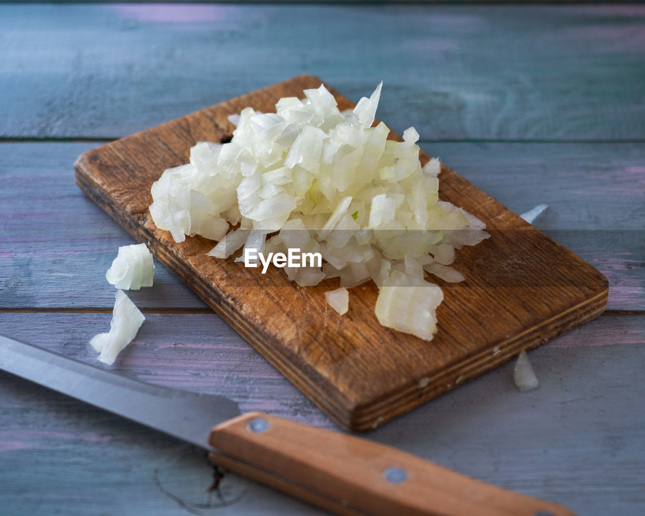 Chopped onions on a cutting board and a kitchen node lie on a wooden table. cooking blank