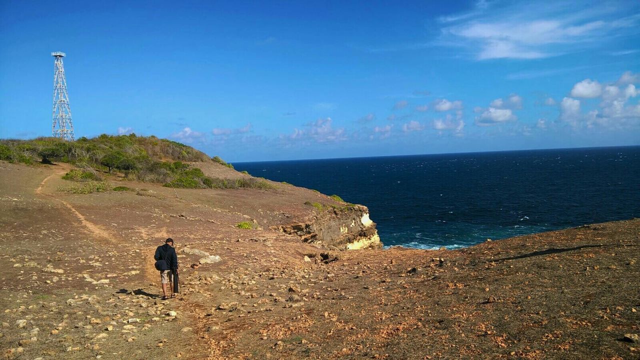 Full length rear view of man walking on mountain by sea against sky