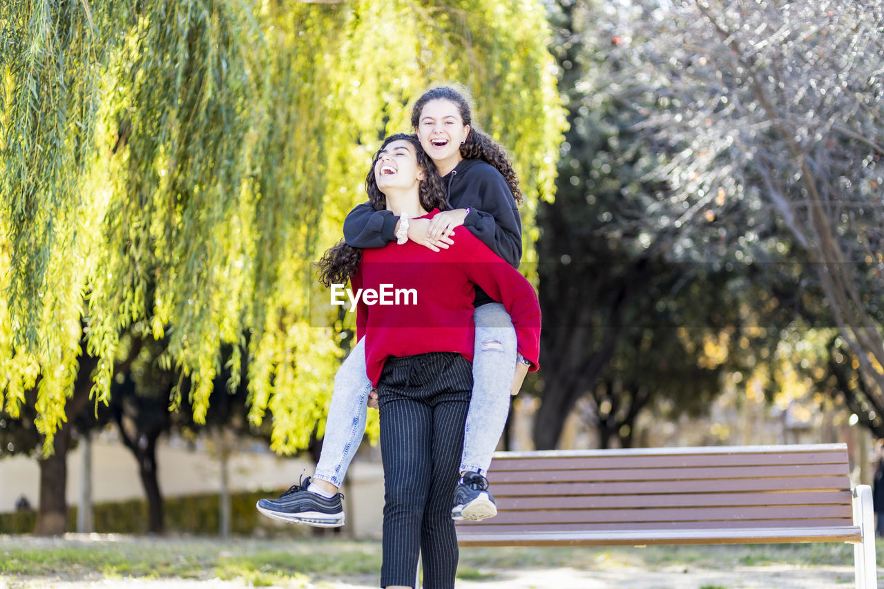 Happy female friend giving piggyback ride to teenager in park