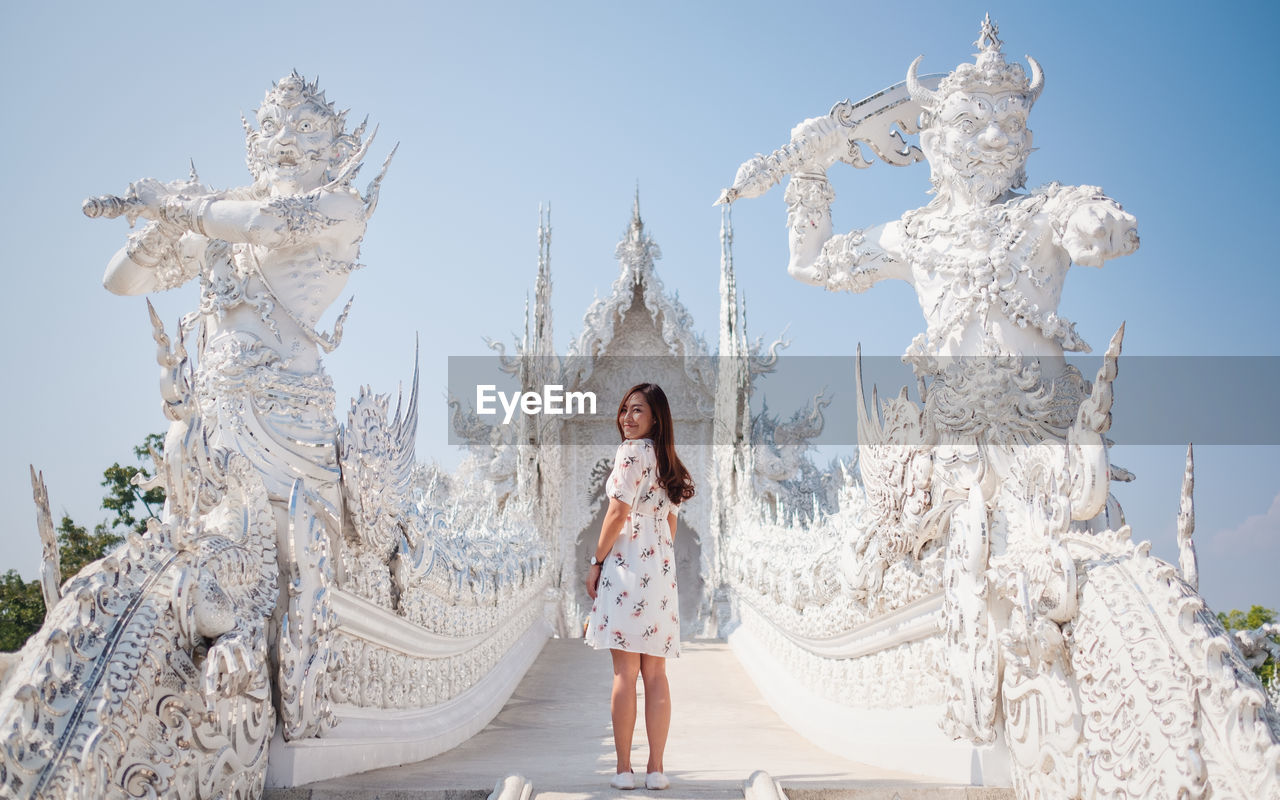 Full length portrait of woman standing by temple against sky