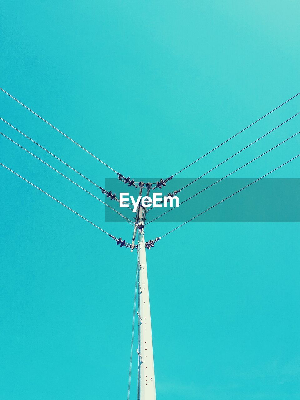 Low angle view of electricity pylon against clear blue sky during sunny day