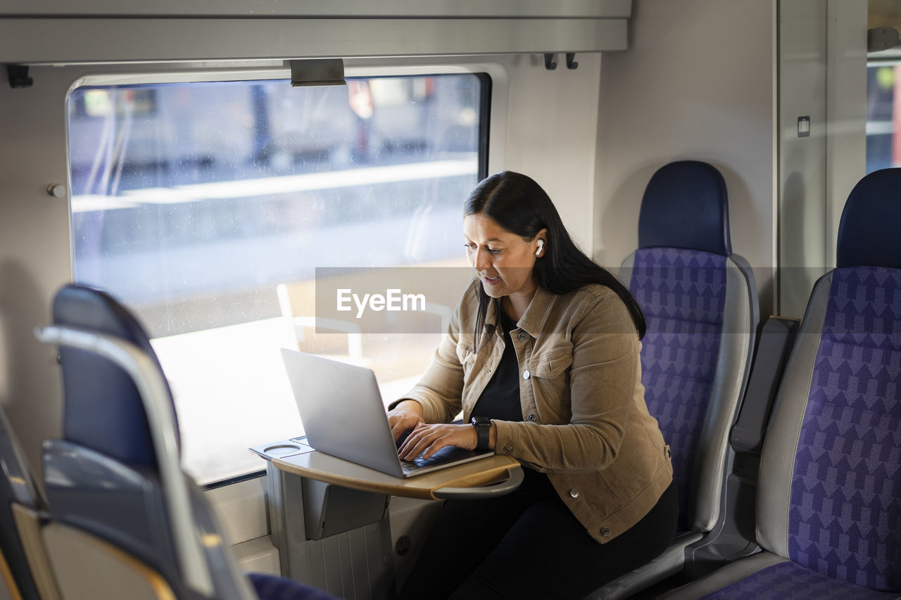 Mid adult woman in train using laptop