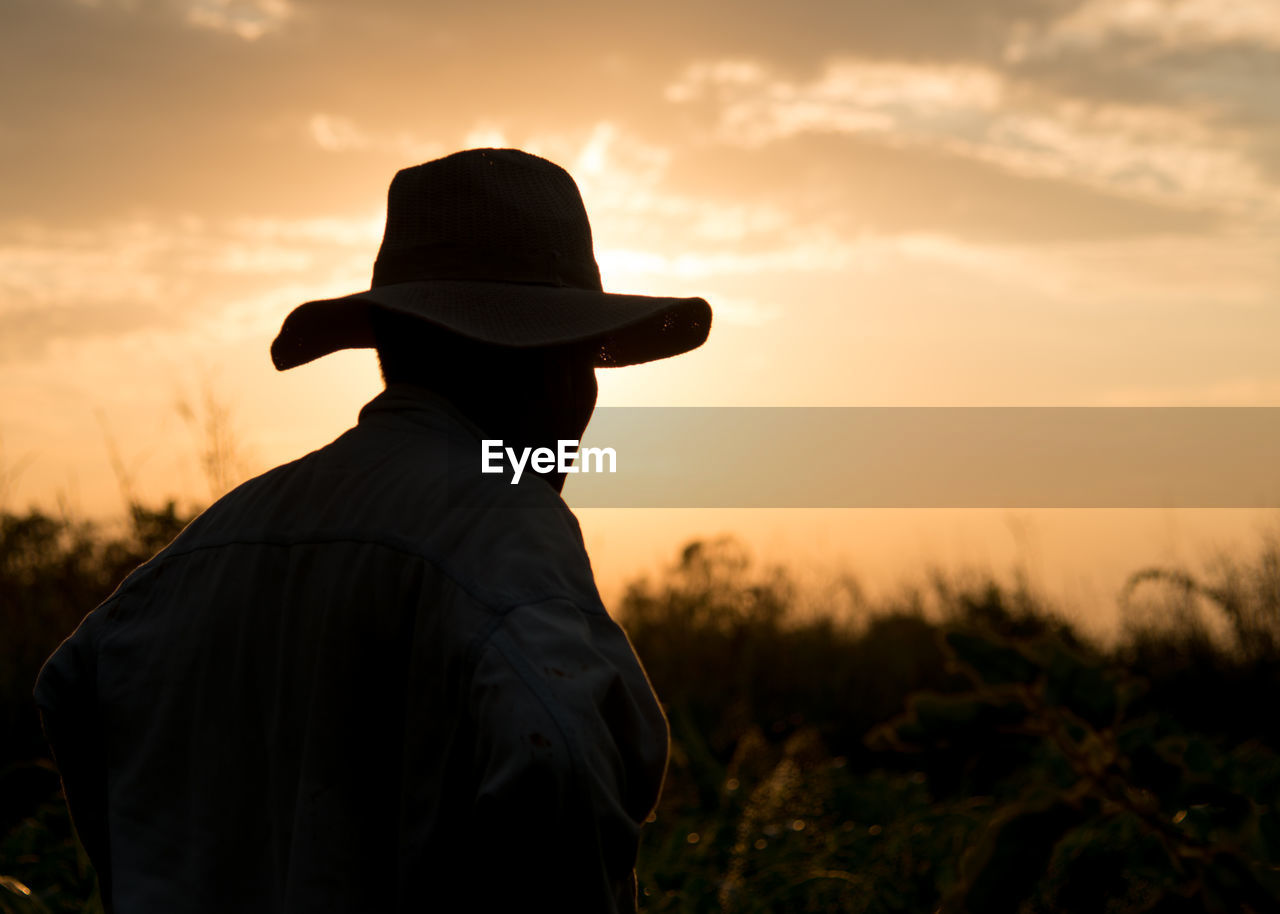 Rear view of silhouette man standing on field against sky during sunset