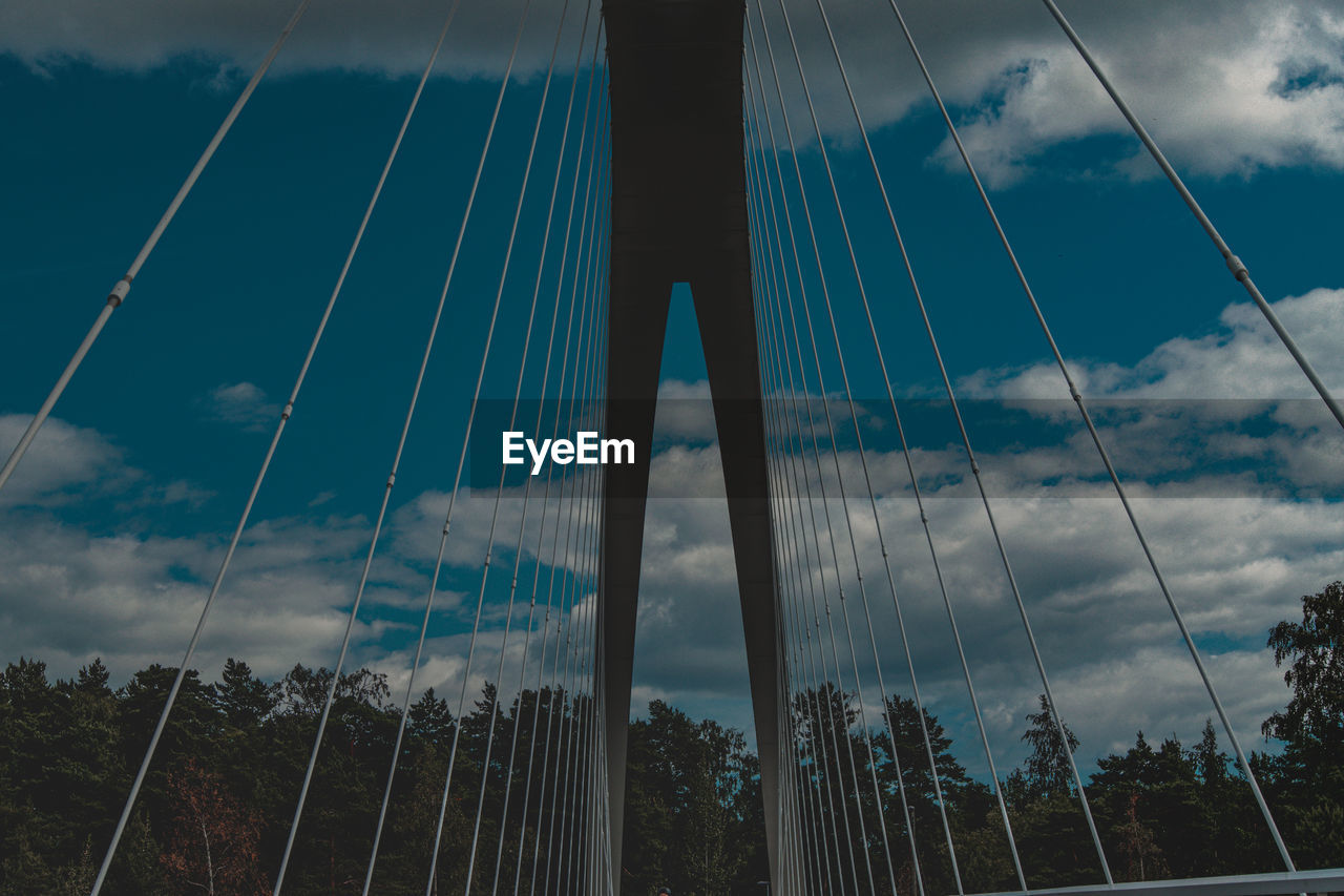 LOW ANGLE VIEW OF SUSPENSION BRIDGE CABLES AGAINST CLOUDY SKY