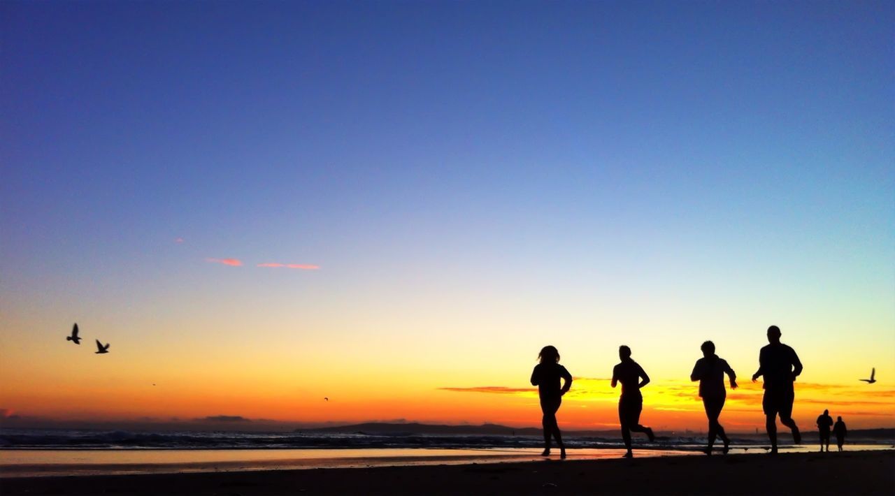 Group of silhouette friends running on beach at sunrise